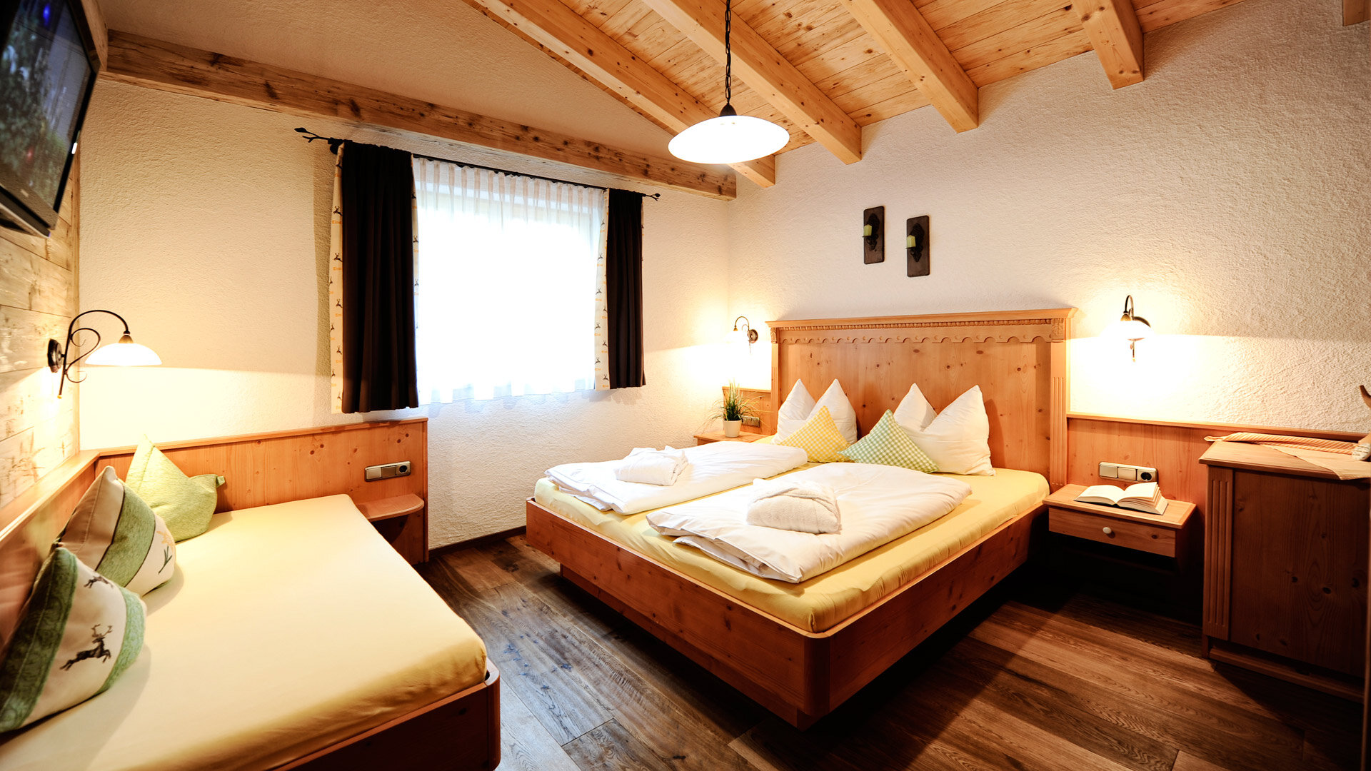 Gemütliches Schlafzimmer mit Doppelbett, Einzelbett und Holzmöbeln im Chalet-Stil.