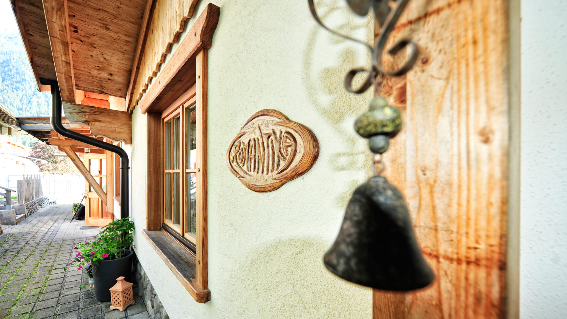 Außenansicht eines Chalets mit Holzschild „Romantika“ und dekorativer Glocke.