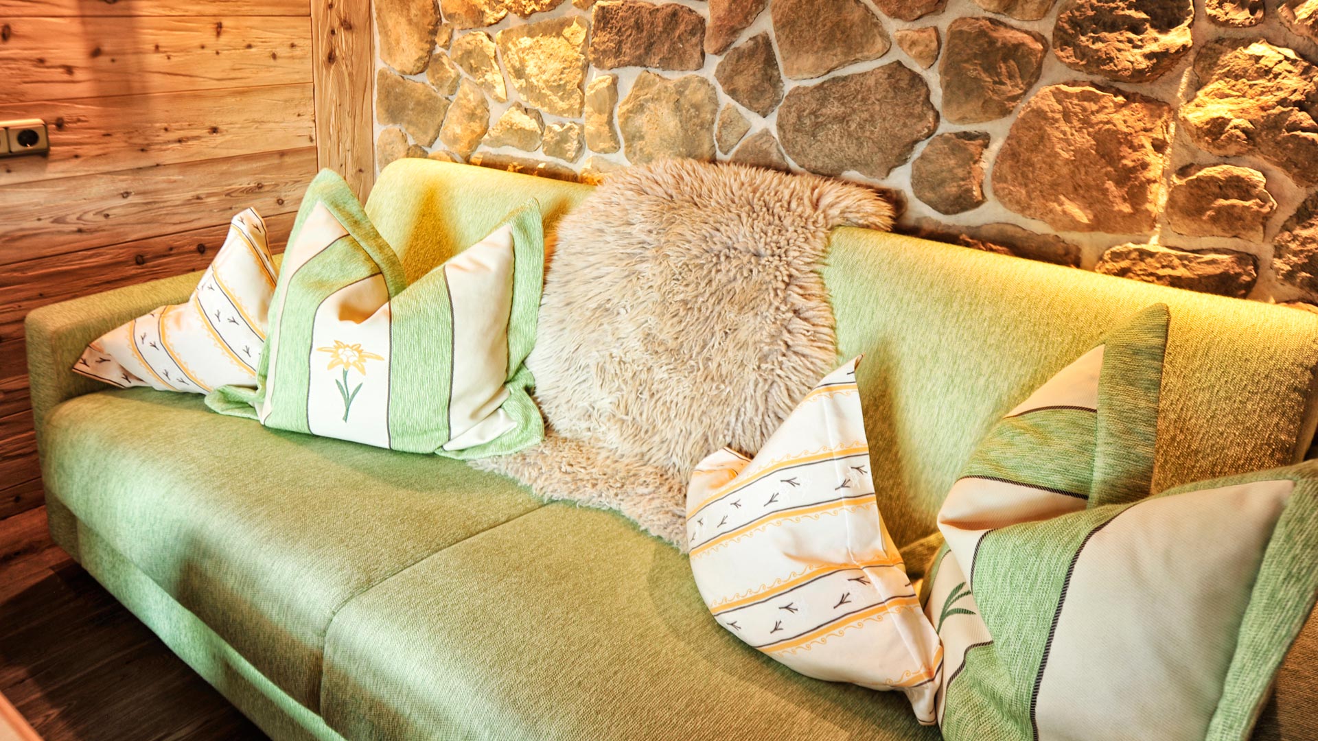 Gemütliches grünes Sofa mit Kissen und Fell vor Steinwand in Chalet-Stube.
