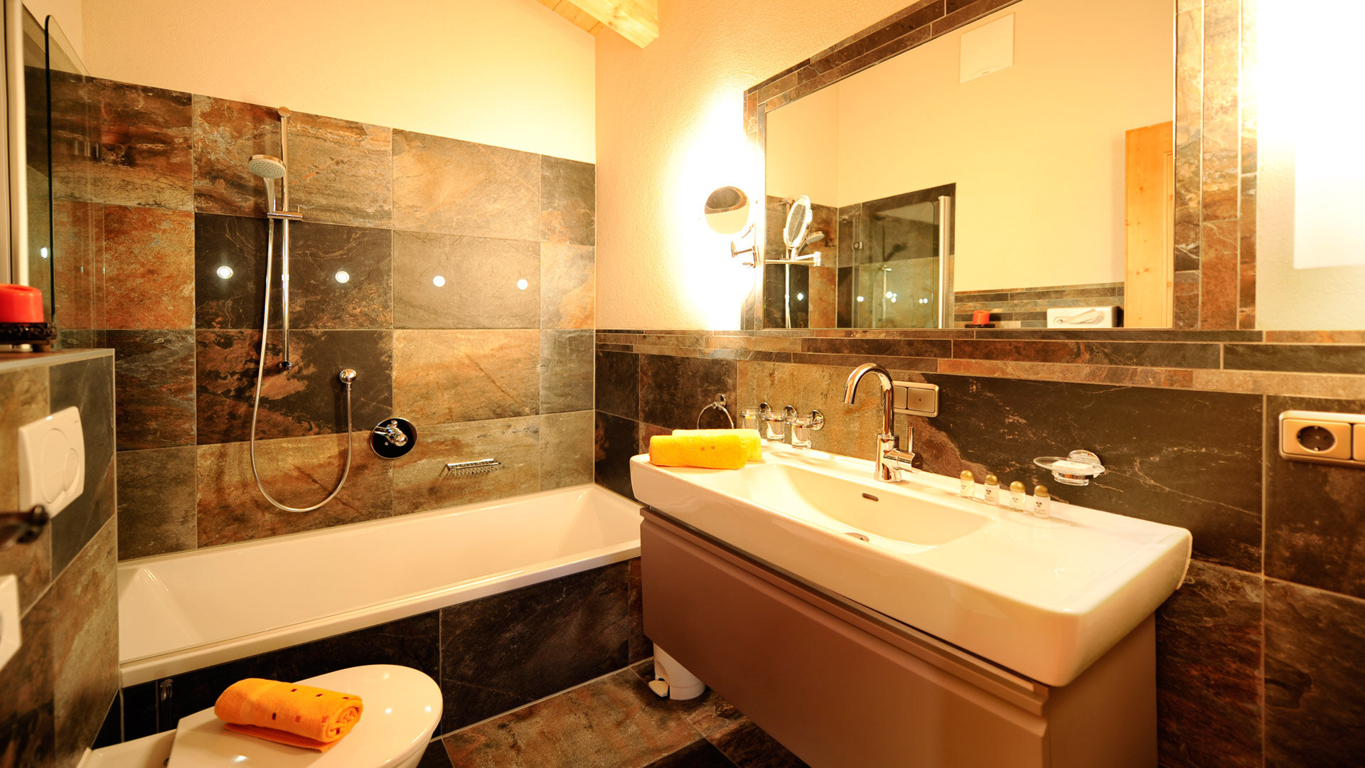 Modernes Bad mit Steinfliesen, Badewanne, großem Spiegel und Waschbecken in gemütlicher Atmosphäre mit warmem Licht.